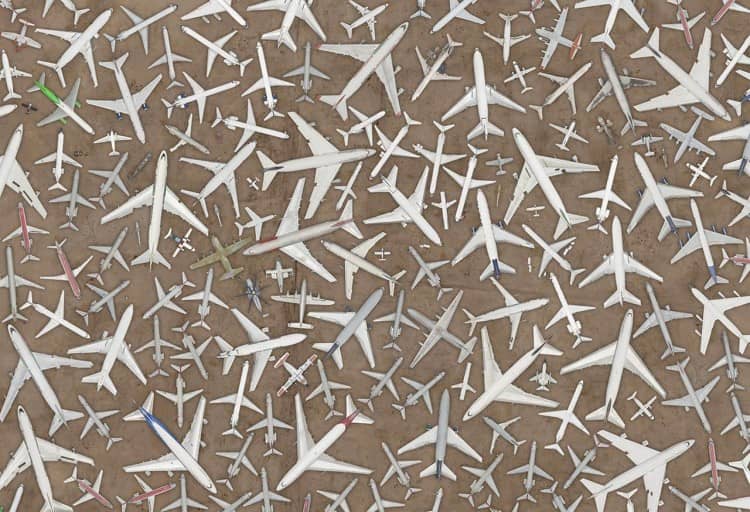 dozens of airplanes and aircrafts in a desert landscape (from above and pointing different directions) forming geometric patterns